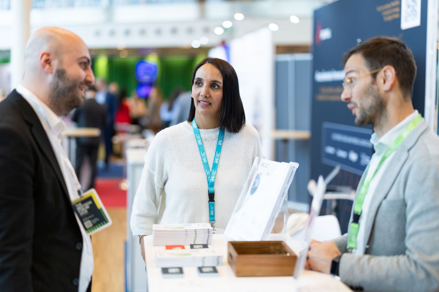 Three professionals networking at an exhibition booth during a business conference.