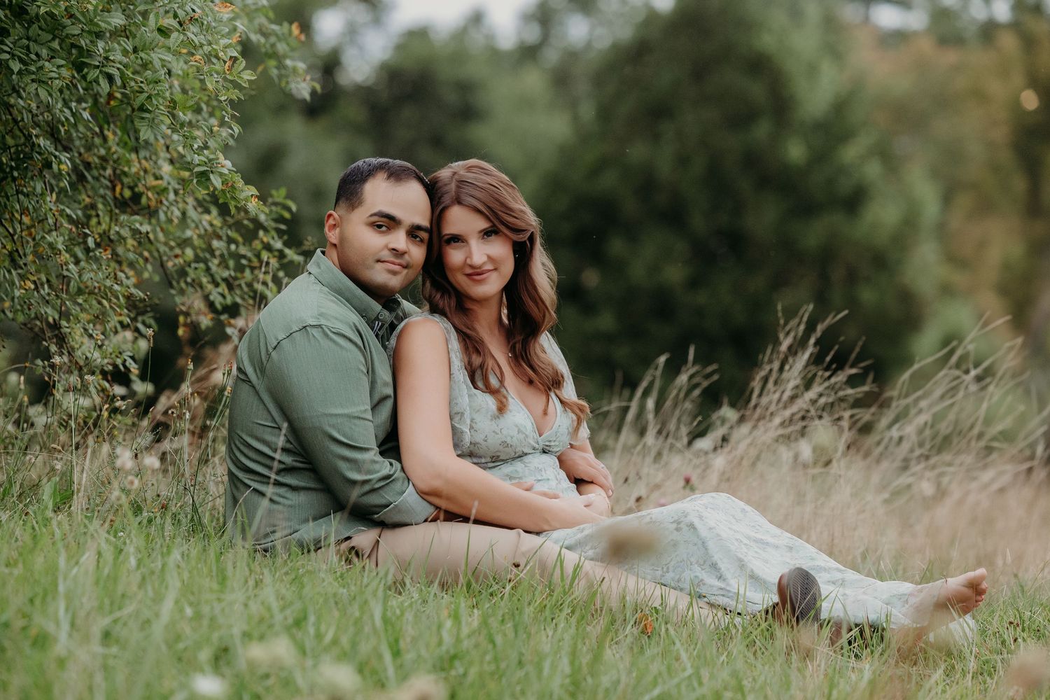 Couple kissing outdoors holding a wicker basket with ultrasound photos and greenery, pregnancy announcement photo.