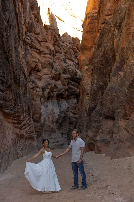 Couple in wedding attire holding hands in a stunning red rock canyon with towering sandstone walls.