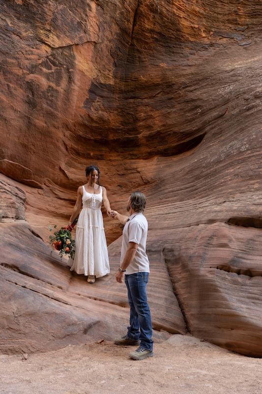 Couple holding hands during outdoor elopement ceremony in a stunning red rock canyon in Utah.