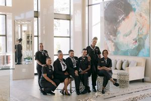 A diverse group of hotel staff in black uniforms posing together in a modern lobby with large artwork.
