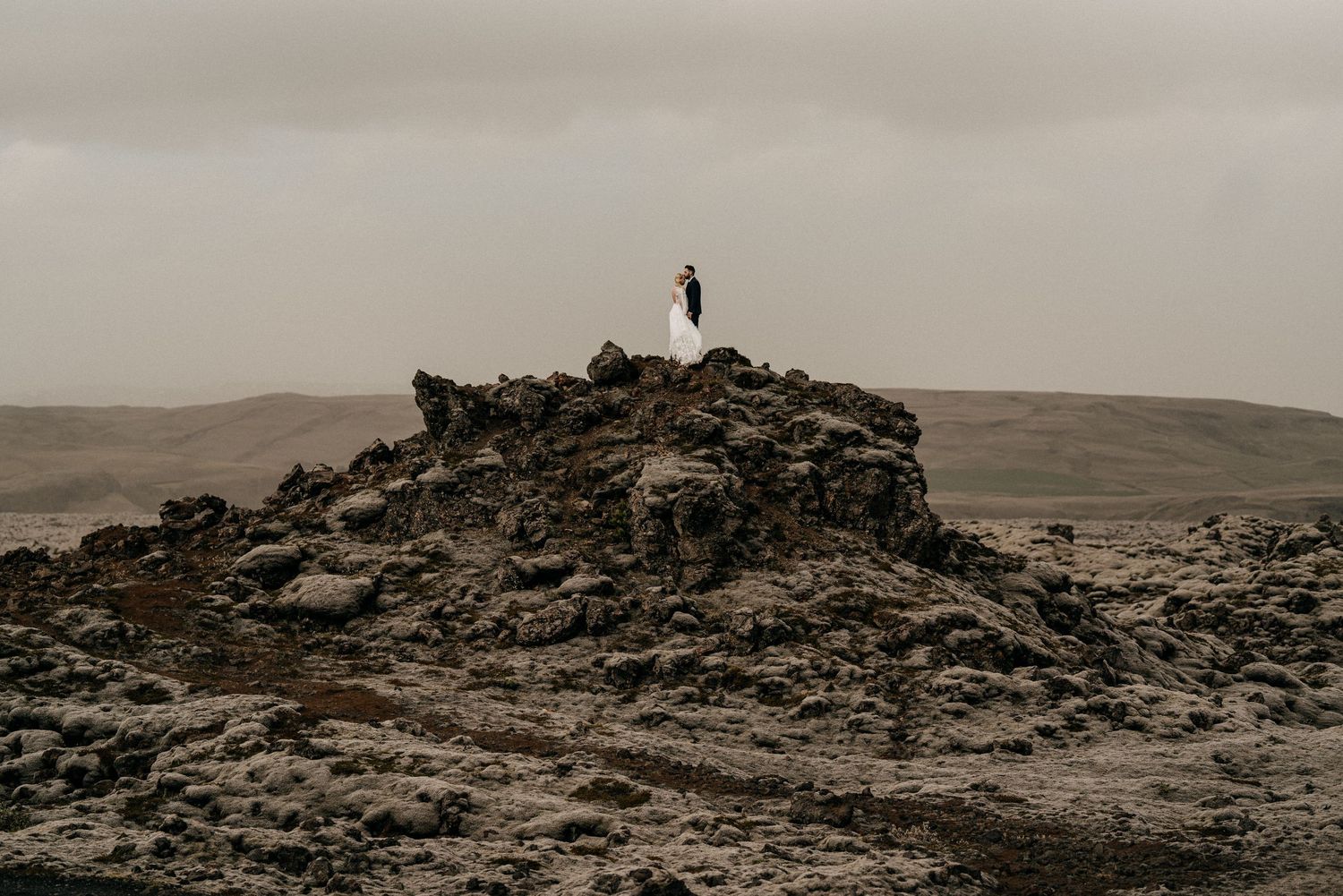 Couple standing atop dramatic volcanic rock formation during moody Iceland elopement ceremony.