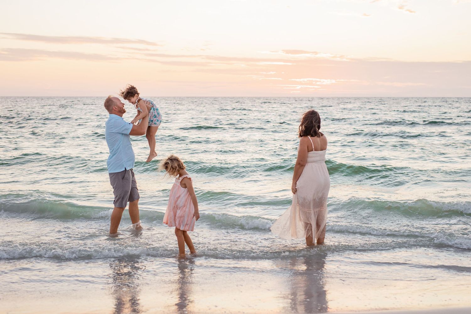 Family playing in ocean waves at sunset during beach photo session.