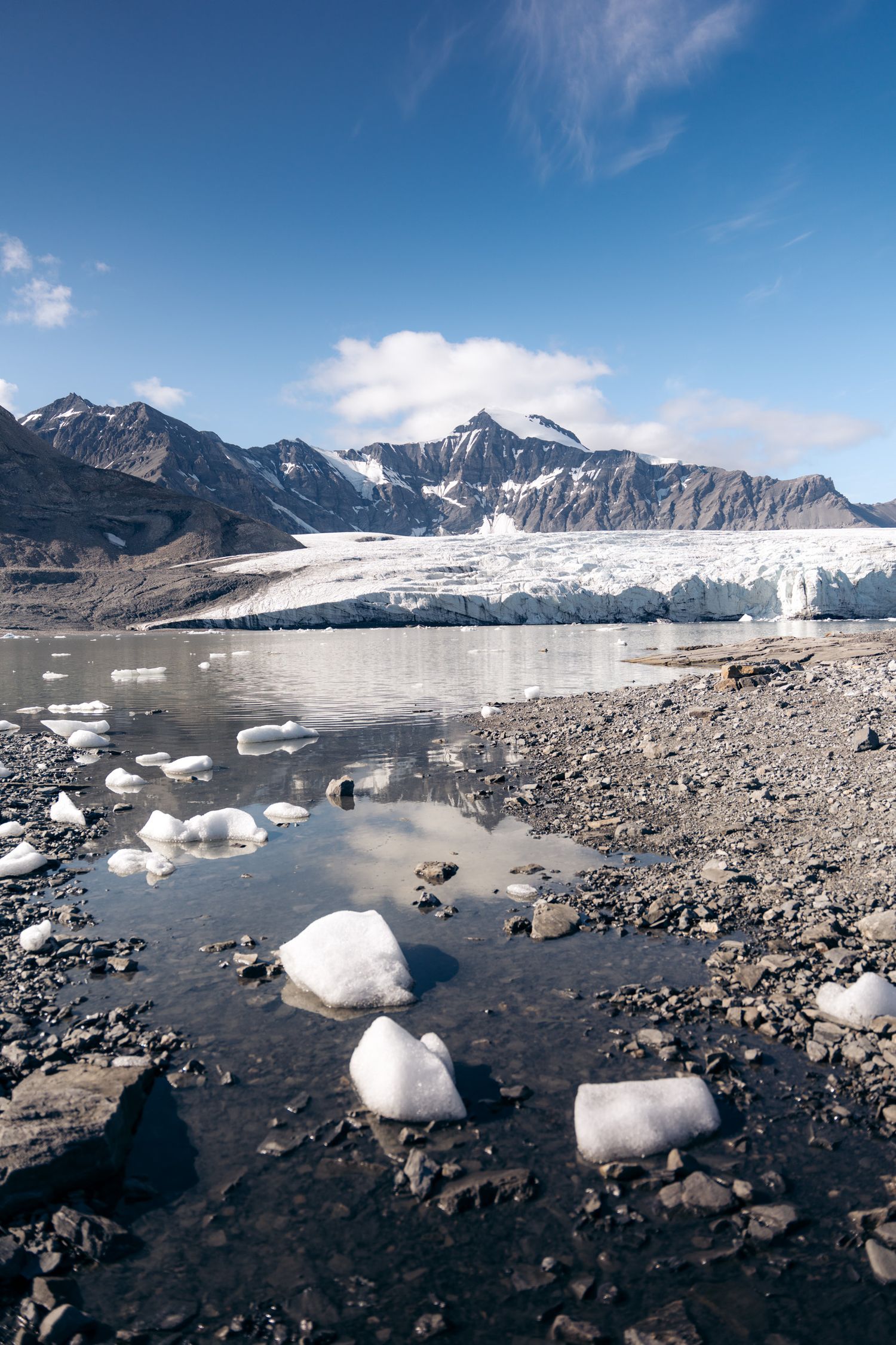 Blocs de glace échoués sur la grève devant un front glaciaire et des sommets enneigés