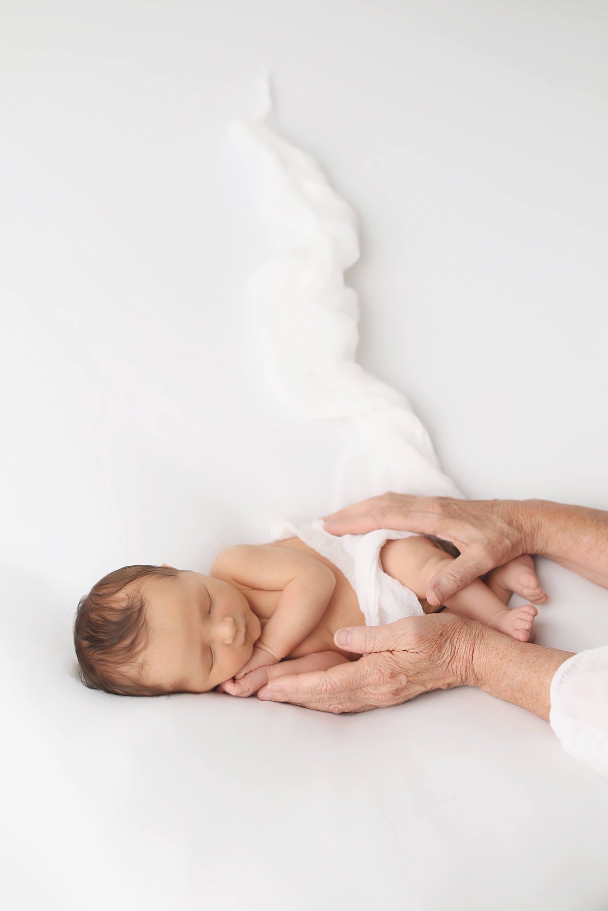 Newborn baby sleeping peacefully in elderly hands with white angel wings on white background.