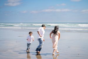 Family of three children playing tag on a sunny beach with ocean waves. Oceanside, CA