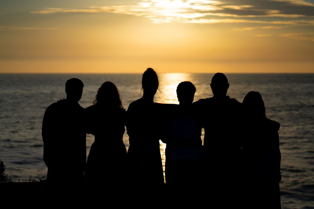 Silhouettes of family of six with arms around each other watching a golden sunset over the ocean. Sunset Cliffs, San Diego, CA