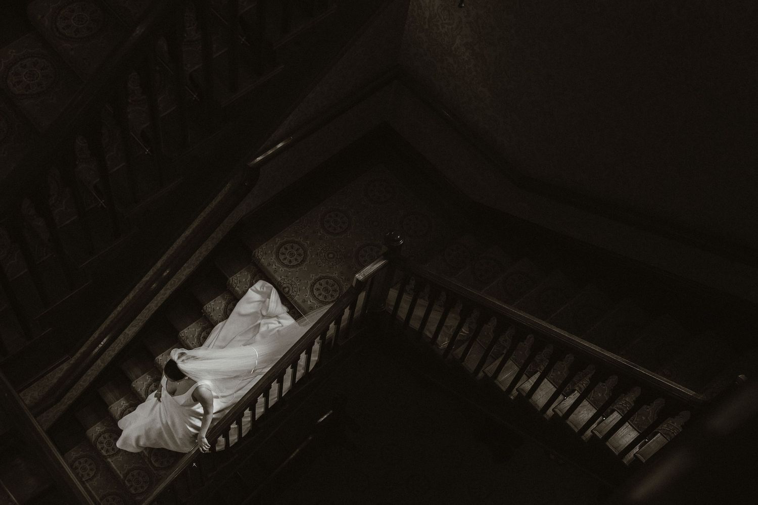 Aerial view of a bride walking down a dark ornate staircase in Kilronan Castle, Co. Roscommon