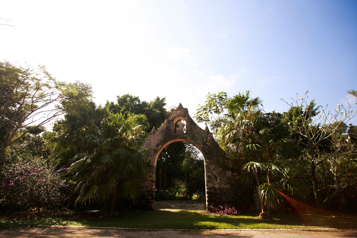 Stone archway entrance framed by palm trees and tropical vegetation in sunlight.