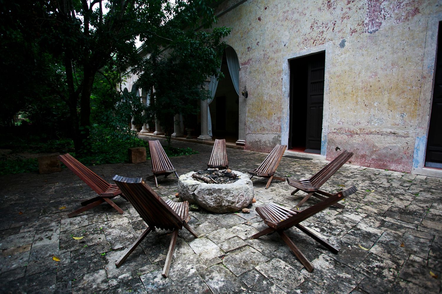 Abandoned stone patio with wooden lounge chairs arranged around a circular fire pit.