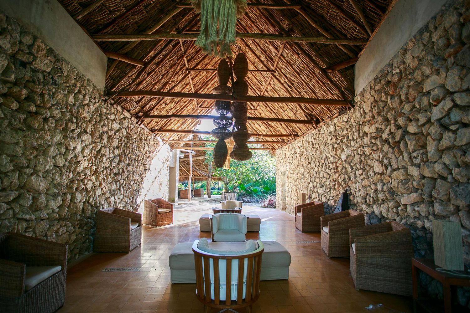 A rustic stone-walled room with thatched roof and comfortable lounge seating arranged around a central space.