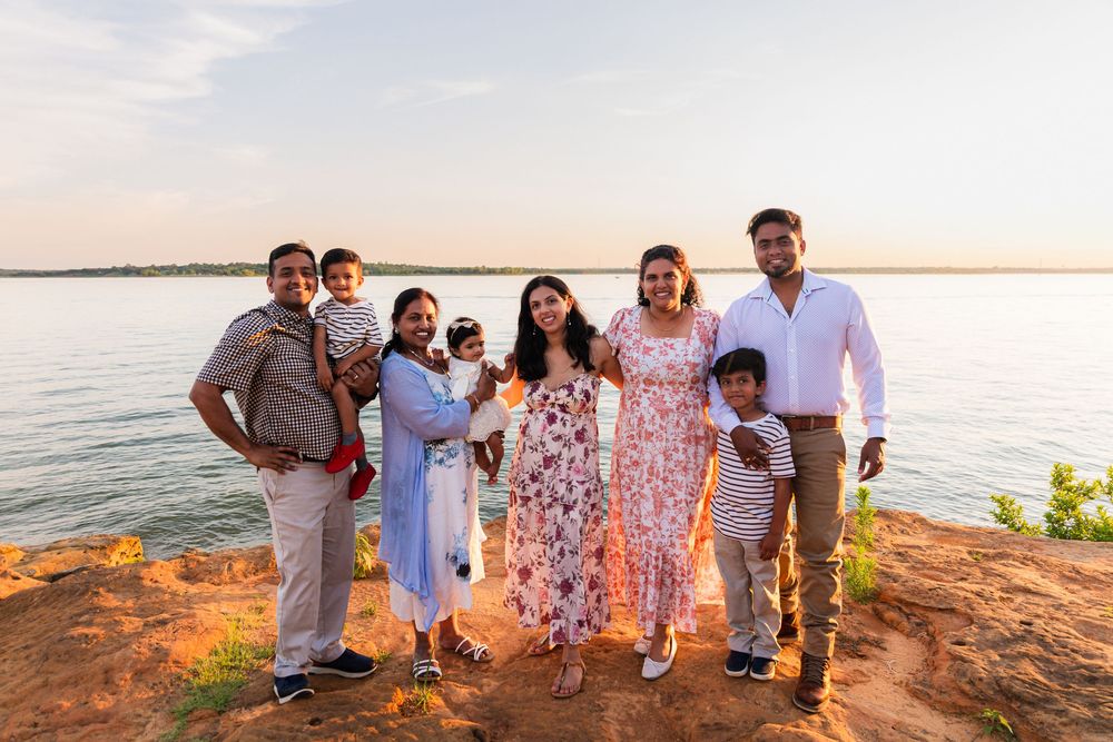 Family of seven posing at sunset on rocky shoreline with calm water in background.