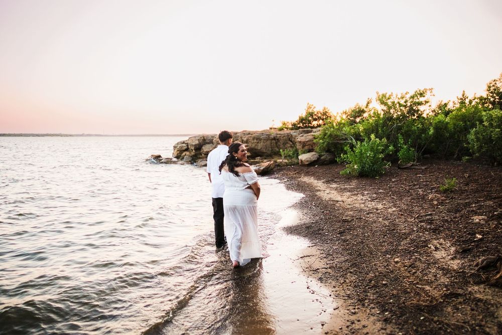 Couple embracing on rocky shoreline at sunset during romantic outdoor wedding photo session.