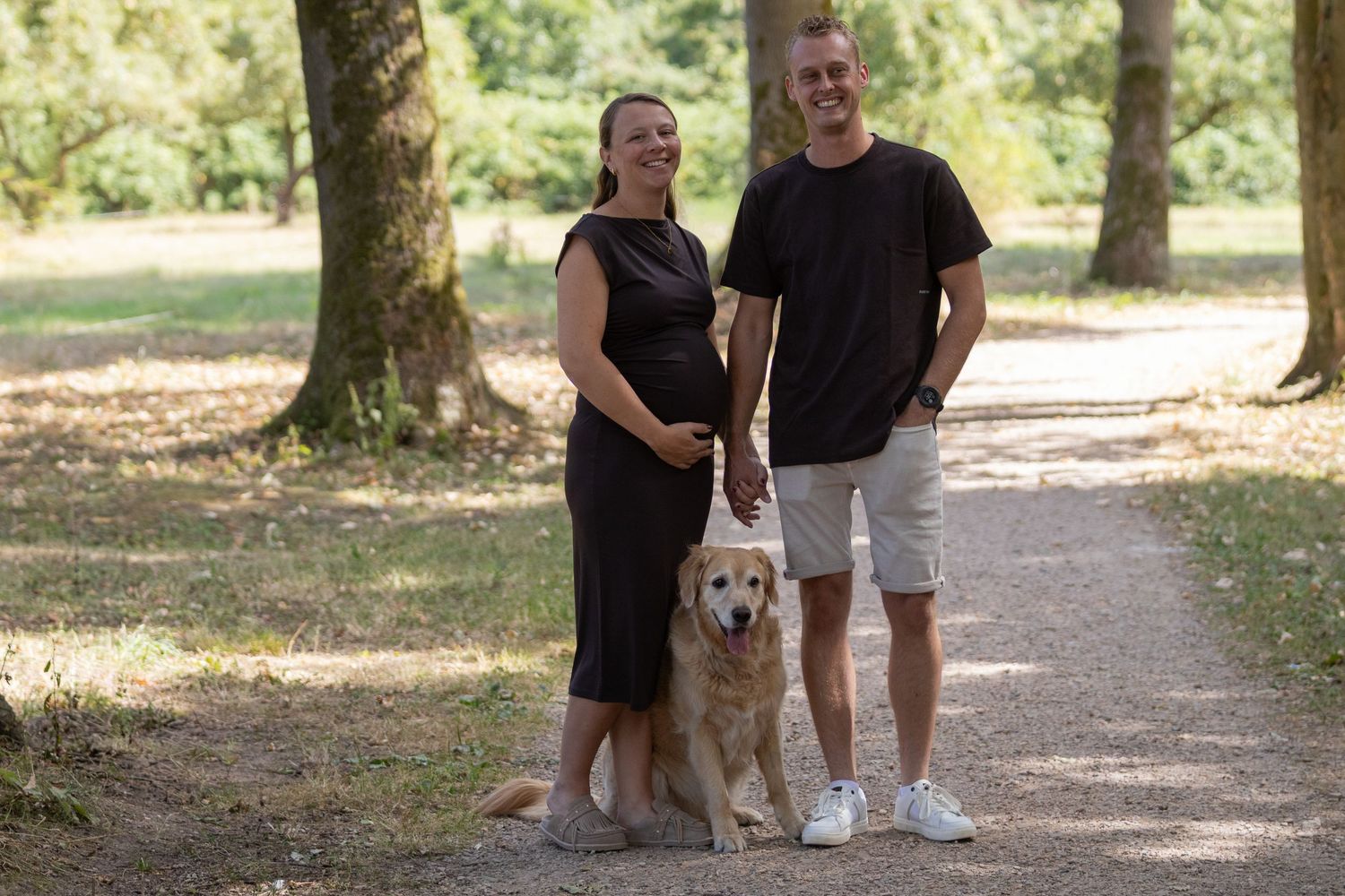 Aanstaand ouderpaar poseert met hun hond op een zonnig bospad.