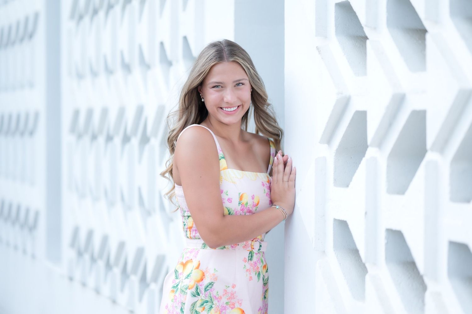Young woman in floral dress smiling against white geometric wall backdrop.