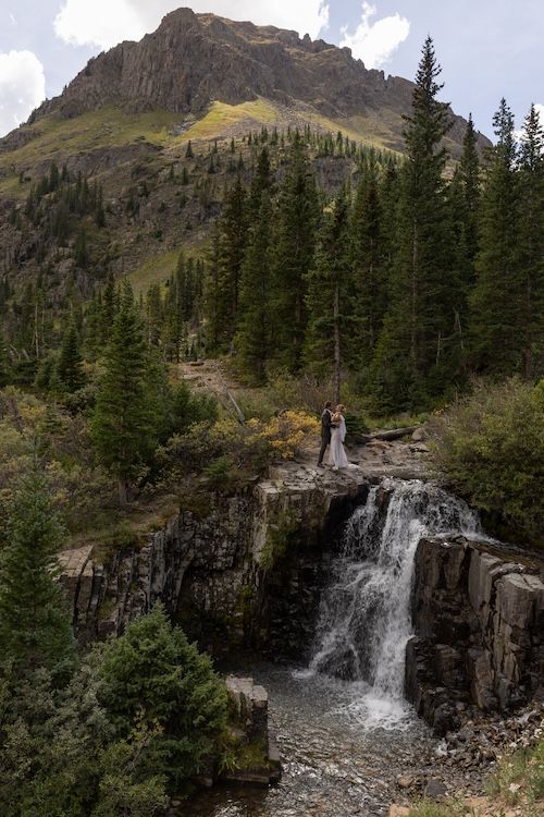 Couple elopes at a stunning mountain waterfall surrounded by pine trees and rocky peaks in Colorado.