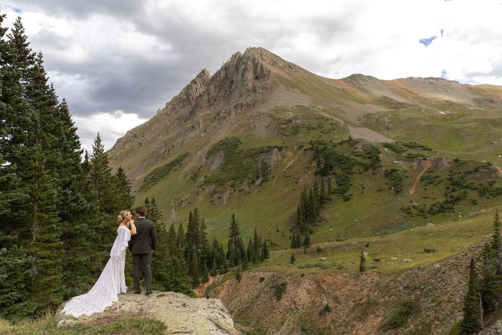 Bride and groom kissing on a rocky overlook with stunning mountain landscape in Colorado during outdoor wedding elopement.