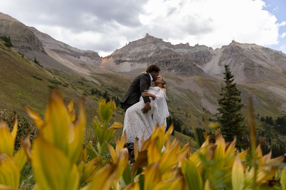 Couple sharing a romantic kiss during mountain elopement surrounded by yellow wildflowers in Colorado.