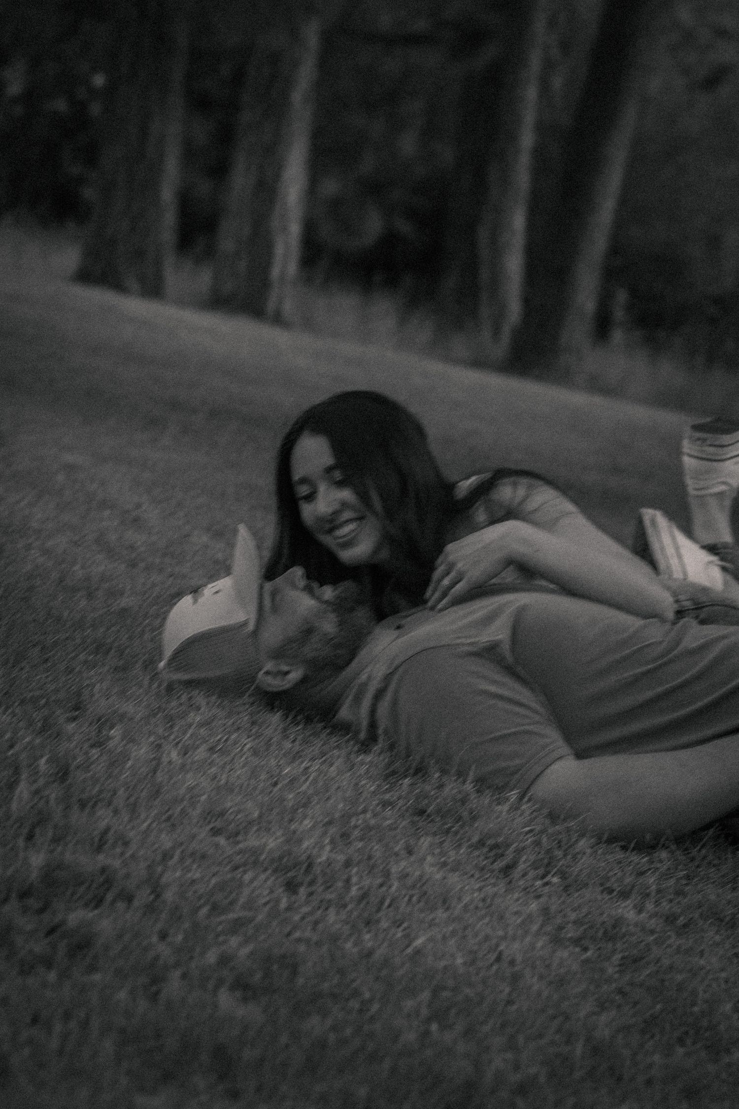 Black and white photo of a smiling couple lying on grass in a park, sharing a tender romantic moment.