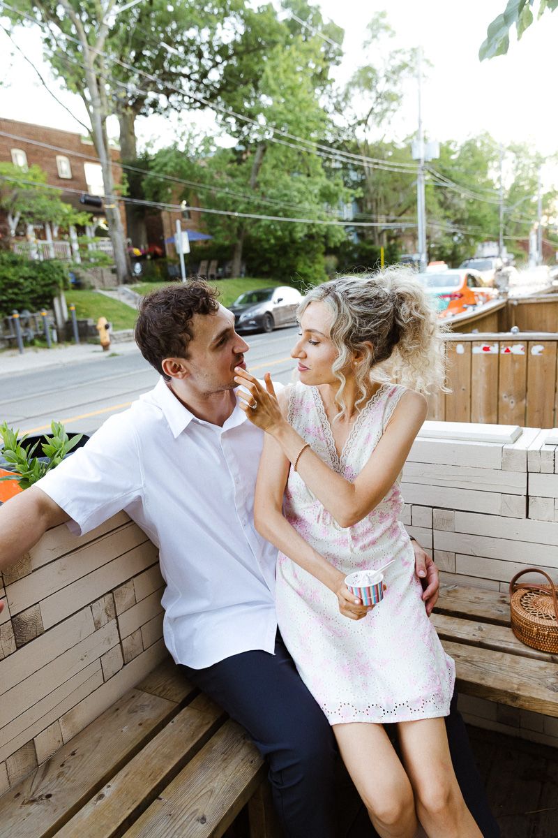 Couple sharing a romantic moment on a wooden bench at an outdoor cafe patio on a sunny summer day.