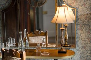 Elegant vintage dressing table with brass lamp, glass bottles, and ornate mirror on floral wallpaper background at Boyne Hill House Estate