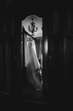 Black and white photo of a white wedding dress hanging in a doorway with a chandelier above in an elegant room at Boyne Hill House