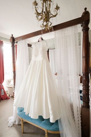 Elegant white satin ball gown wedding dress hanging on a four-poster bed in a romantic bridal suite in Boyne Hill House Estate, Co. Meath
