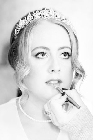 Black and white photo of a bride wearing a tiara and pearl necklace having her makeup applied by a makeup artist at Boyne Hill House Estate