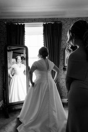 Bride in white gown views reflection in full-length mirror, in elegant black and white wedding photo at Boyne Hill House