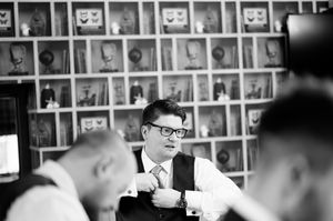 Black and white photo of grooms adjusting his tie at a wedding preparation gathering at Boyne Hill House