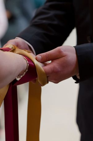 Close-up of hands tying gold and burgundy ribbon in a handfasting wedding ceremony ritual at Boyne Hill House Estate, Co. Meath