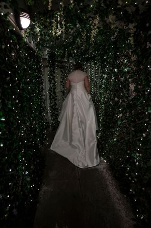 Bride in white wedding gown walking through a magical ivy tunnel adorned with twinkling fairy lights at Boyne Hill House Estate, Co.Meath