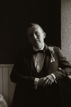 Black and white portrait of a groom in a tuxedo with boutonniere, posing in dramatic lighting at Boyne Hill House Estate