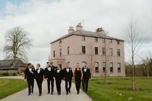 Wedding party in black tuxedos walks along a path in front of Boyne Hill House Estate, Co. Meath in Ireland.