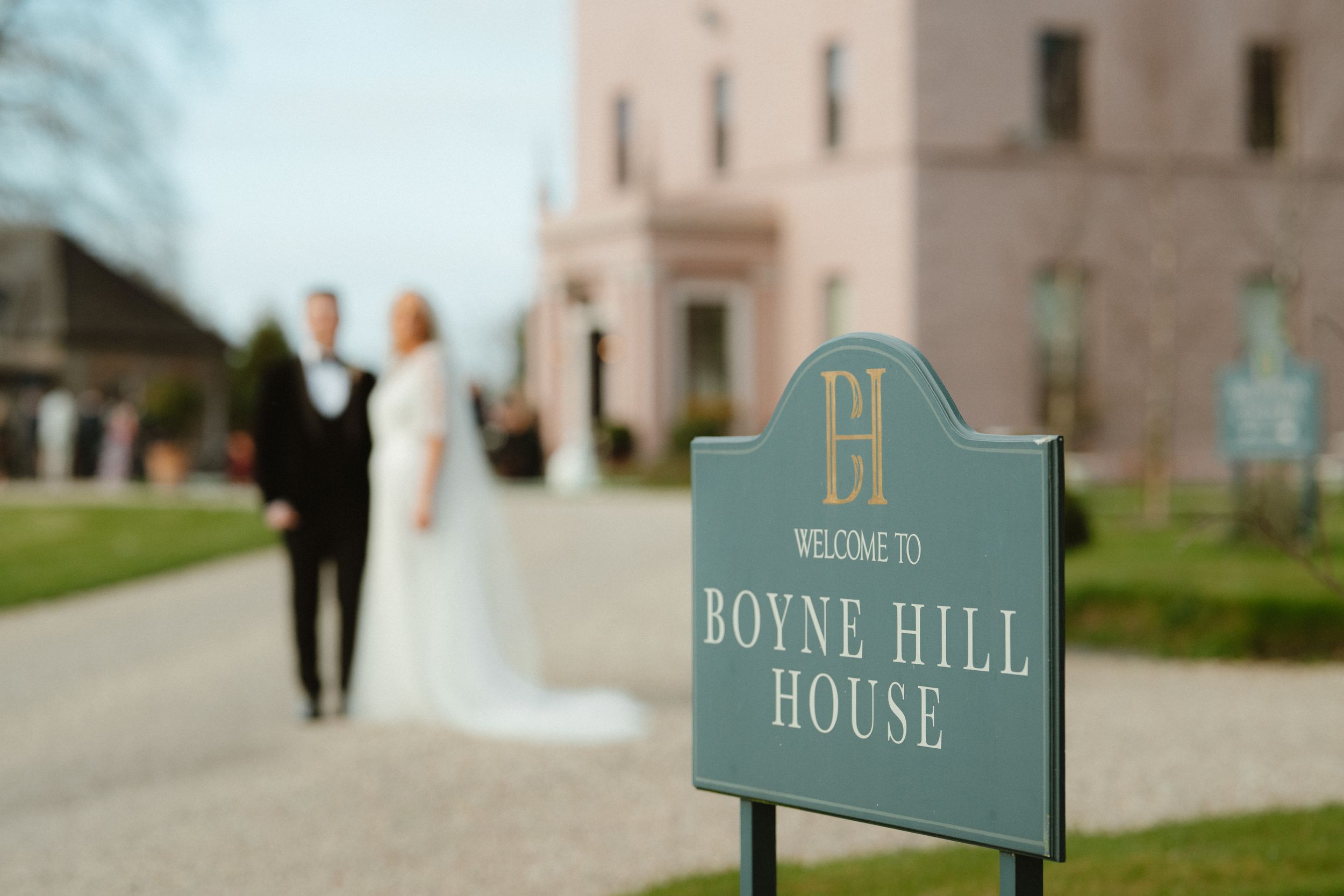 Wedding couple poses behind Boyne Hill House welcome sign at elegant Irish country house venue.
