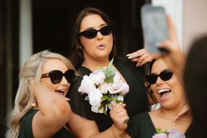 Three bridesmaids in green dresses and sunglasses laughing and posing for a selfie while holding a pink bouquet Boyne Hill House Estate