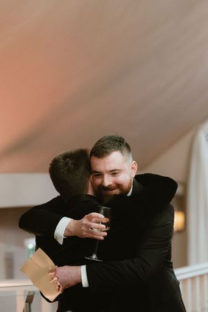 Two men in black suits share a warm hug at a wedding reception at Boyne Hill House Estate
