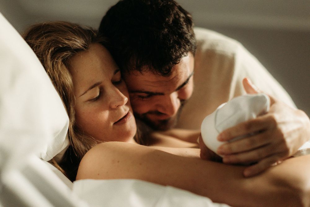 A couple tenderly cradles their newborn baby together in a hospital bed after childbirth.