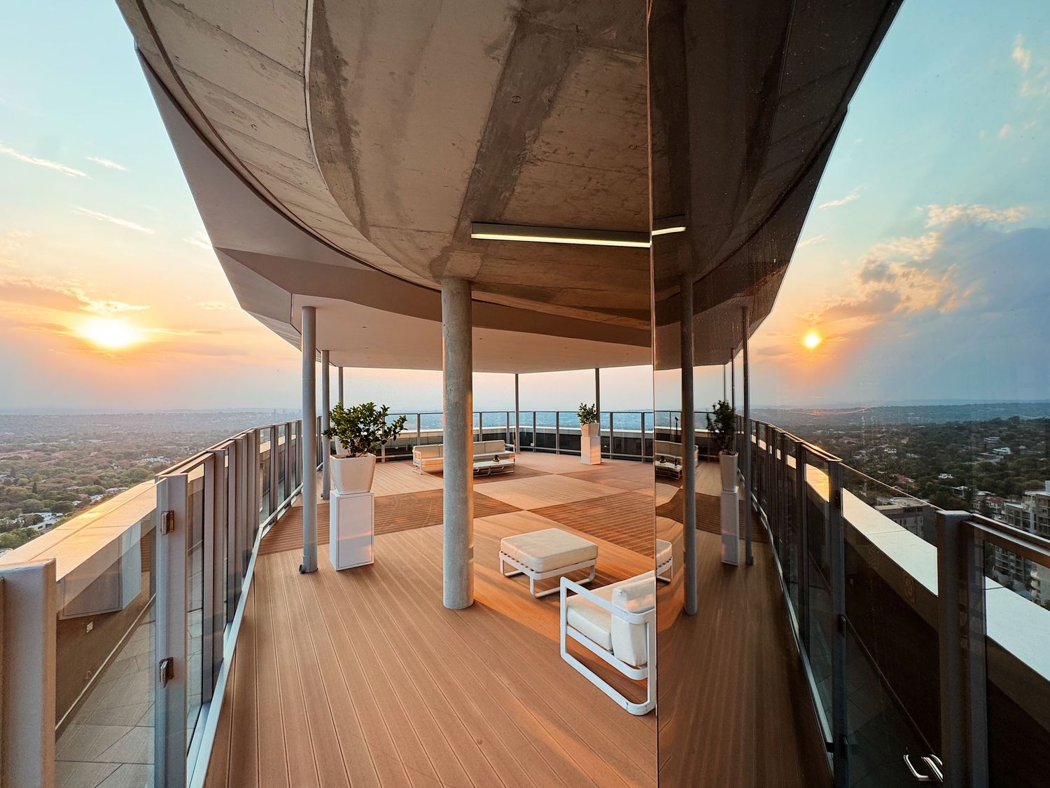 Stunning rooftop terrace with wooden deck, modern furniture, and panoramic city views at sunset.