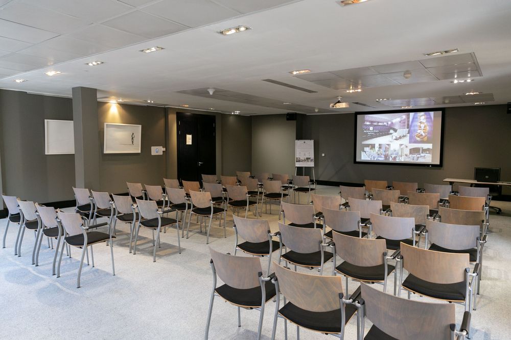 Modern conference room with rows of chairs facing a large projection screen, ideal for corporate events.