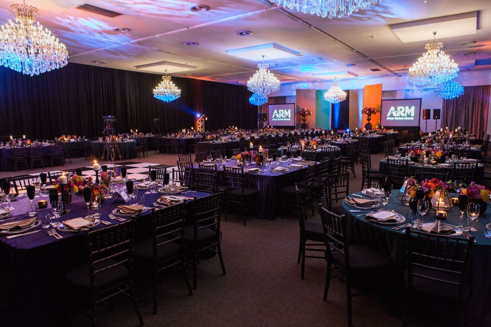 Elegant ARM event banquet hall with crystal chandeliers, black tables, colorful centerpieces, and blue ambient lighting.