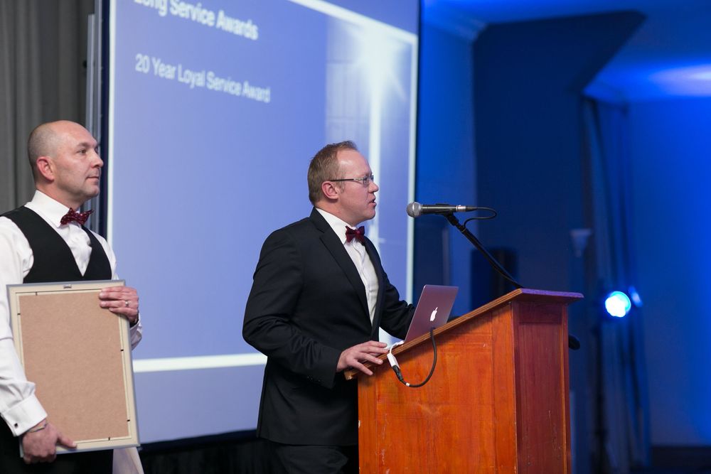 Two men presenting a 25 Year Loyal Service Award at a corporate awards ceremony on stage.
