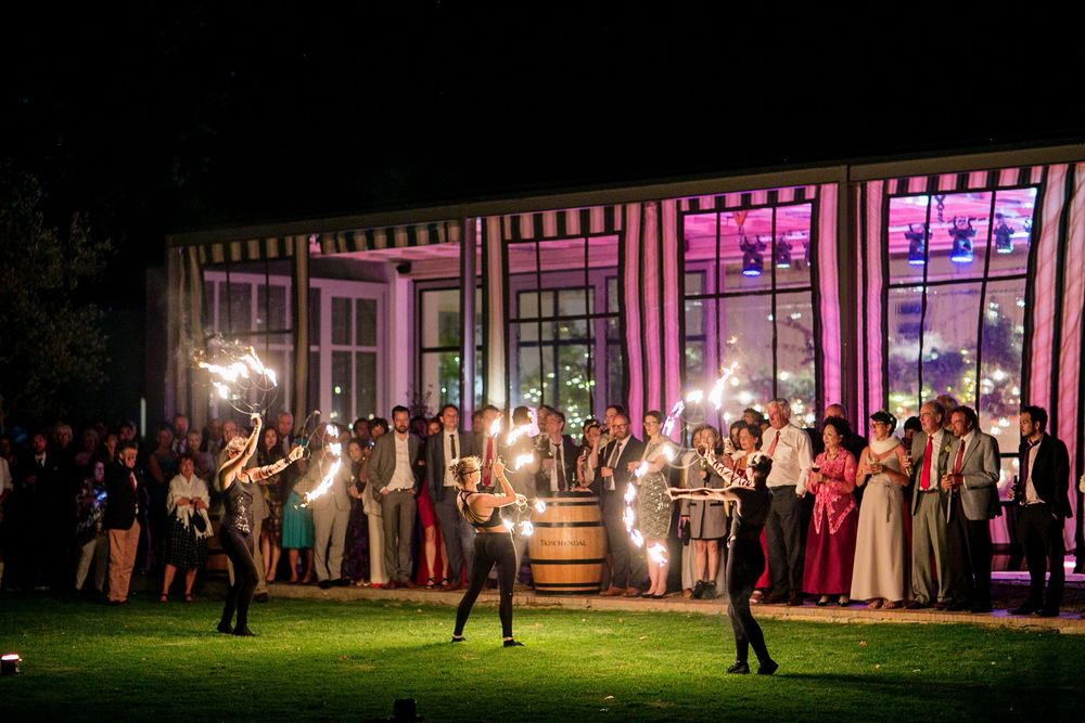 Elegant outdoor evening wedding reception with guests holding sparklers near a striped pavilion at night.