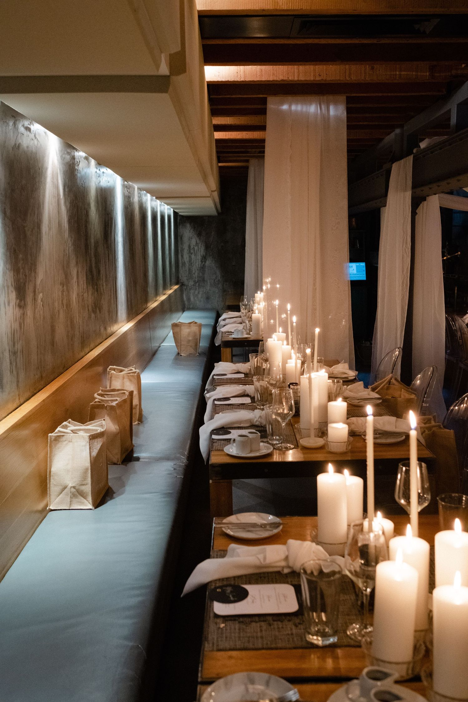 Elegant candlelit restaurant with long dining table, white candles, place settings, and soft draping curtains in warm ambiance.