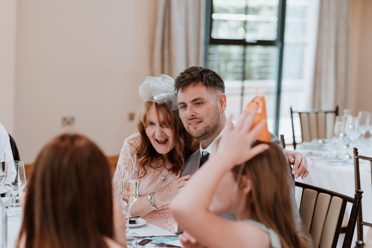 Couple laughing and posing for a photo at a wedding reception dinner table with champagne glasses.