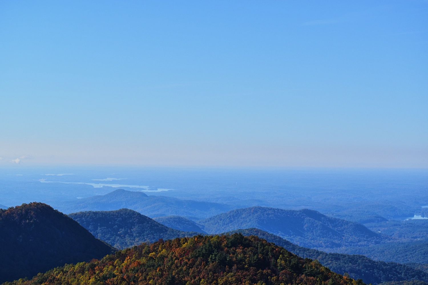 Aerial view of Blue Ridge Mountains with colorful autumn foliage under a clear blue sky stretching to the horizon.