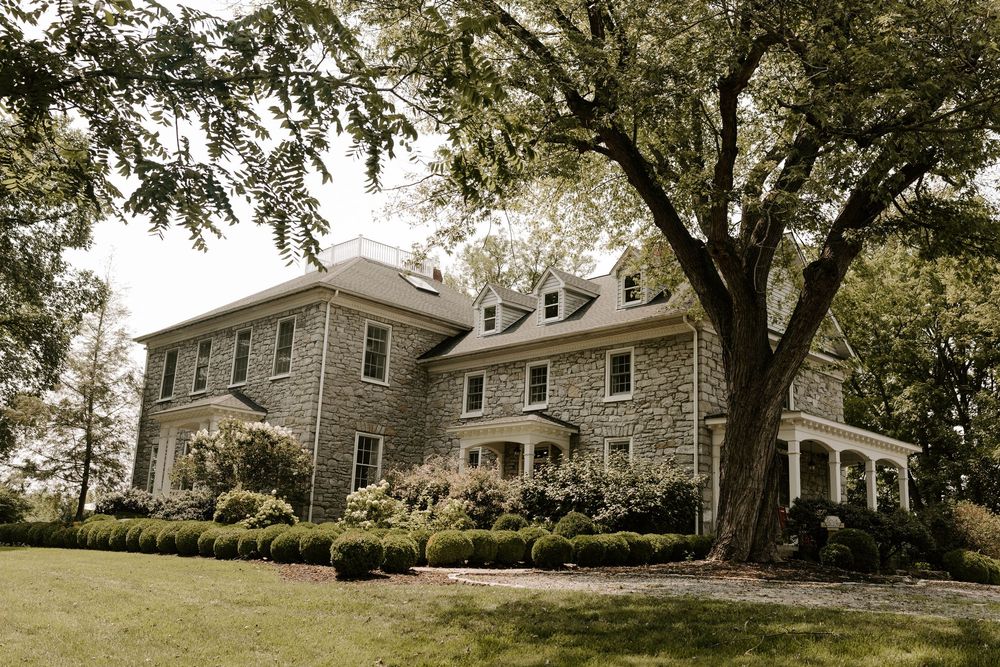 Elegant stone manor house surrounded by mature trees and manicured hedges on a lush green lawn.