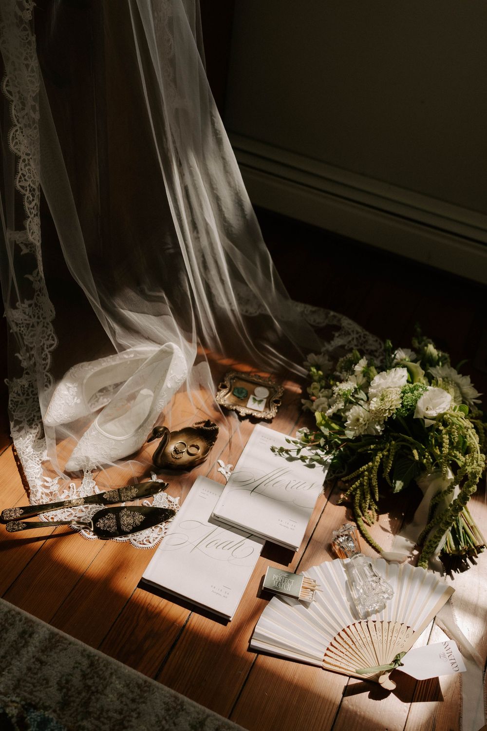 Flat lay of wedding details including veil, bouquet, heels, stationery, and fan in warm natural light.