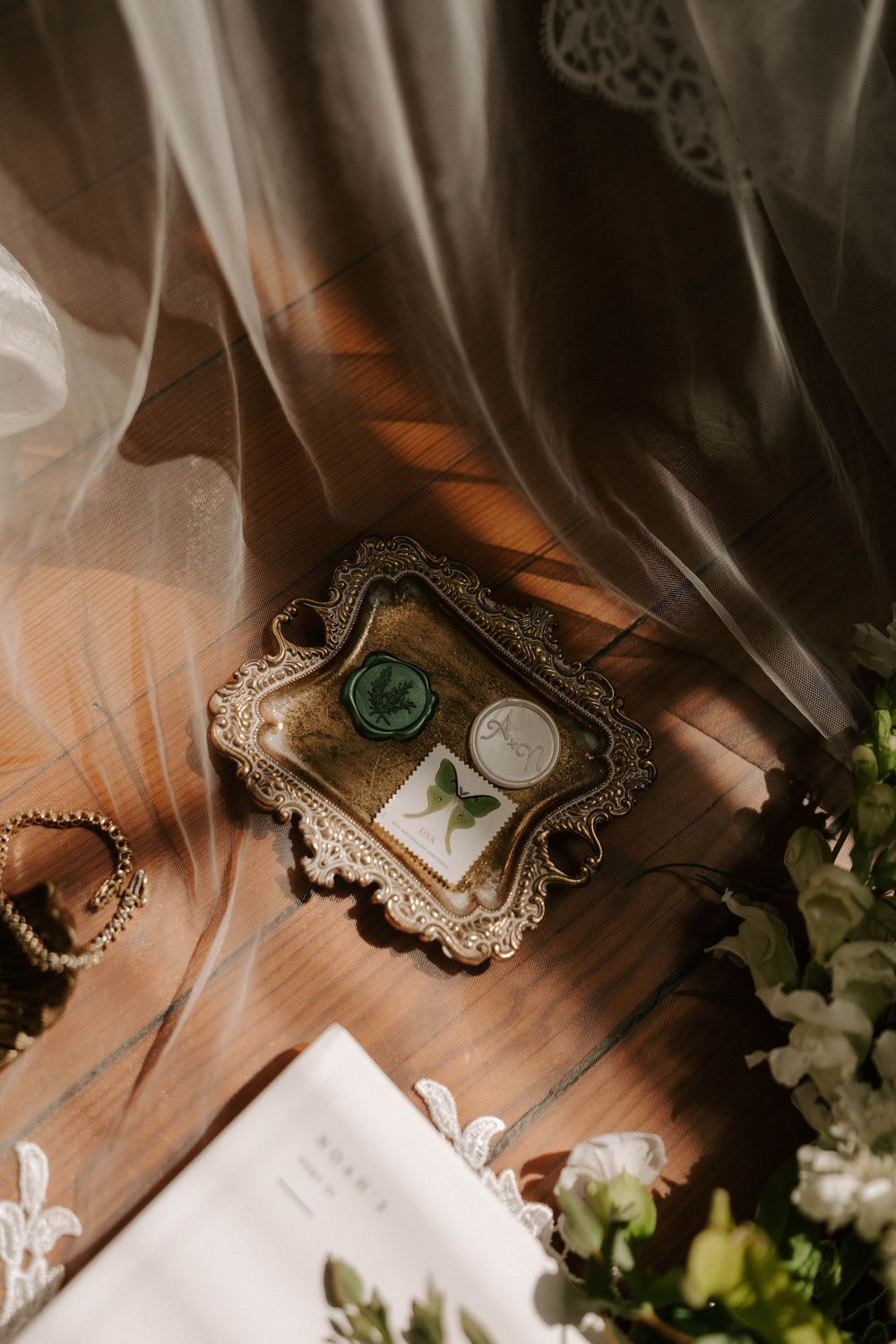 Vintage gold tray with green wax seal and botanical details on wooden floor with soft drapery.