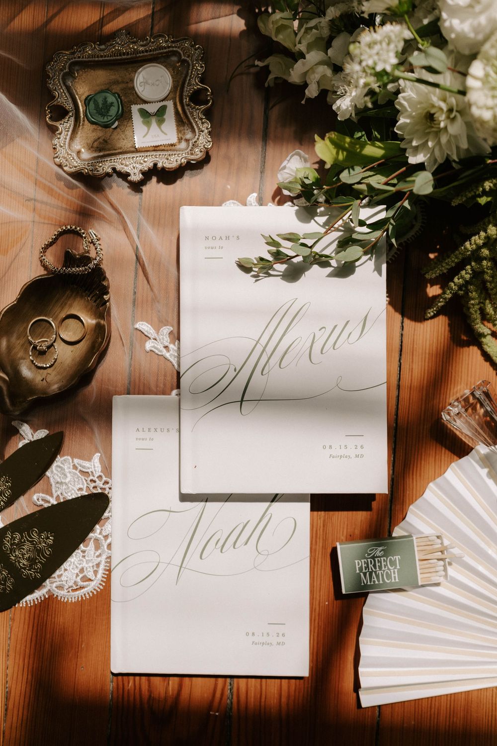 Elegant wedding stationery flatlay featuring calligraphy vow books for Alexus and Noah on a wooden surface.